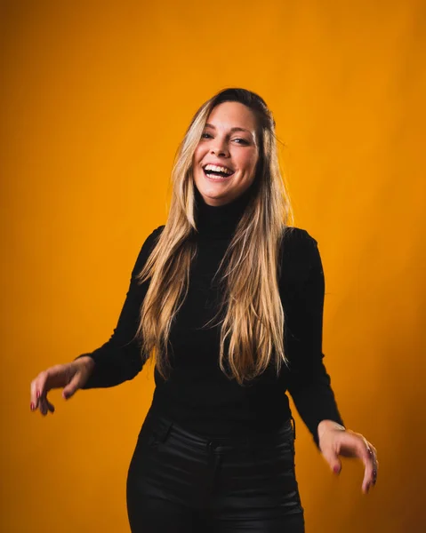 Smiling girl with blond hair roots born looking at the camera wearing black shirt and pants with orange background. — Stock Photo, Image