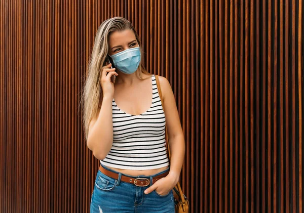 Donna in maschera in città utilizzando il suo cellulare durante la pandemia di coronavirus — Foto Stock