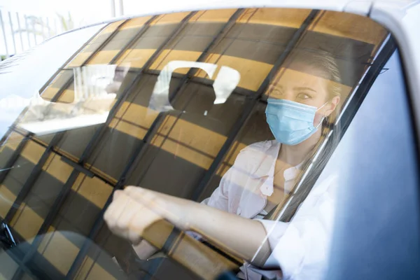 Женщина в маске водит машину во время пандемии коронавируса — стоковое фото