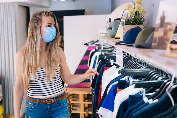Vrouw met masker winkelen in een kledingwinkel in de coronavirus pandemie — Stockfoto