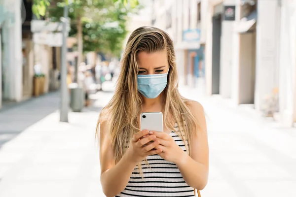 Donna in maschera in città utilizzando il suo cellulare durante la pandemia di coronavirus — Foto Stock