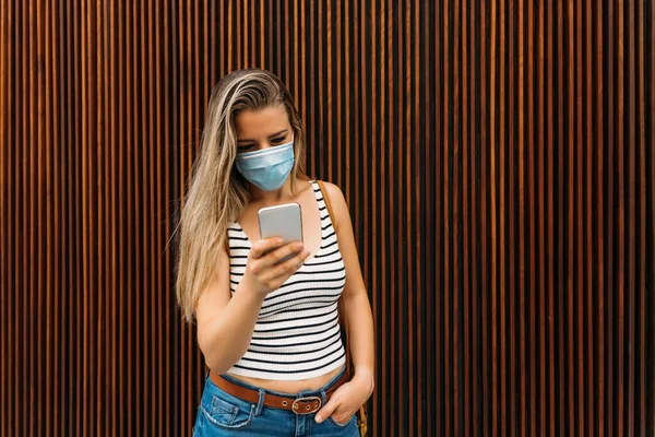 Donna in maschera in città utilizzando il suo cellulare durante la pandemia di coronavirus — Foto Stock