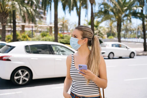 Donna in maschera in città utilizzando il suo cellulare durante la pandemia di coronavirus — Foto Stock