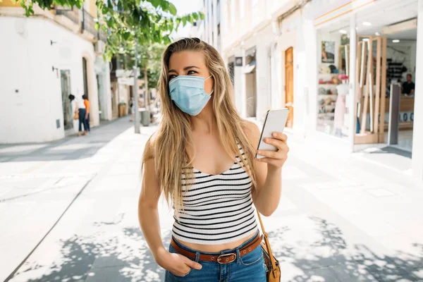 Donna in maschera in città utilizzando il suo cellulare durante la pandemia di coronavirus — Foto Stock