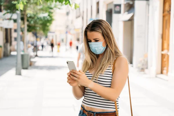 Donna in maschera in città utilizzando il suo cellulare durante la pandemia di coronavirus — Foto Stock