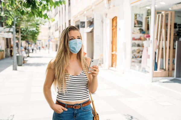 Женщина в маске в городе с помощью мобильного телефона во время пандемии коронавируса — стоковое фото