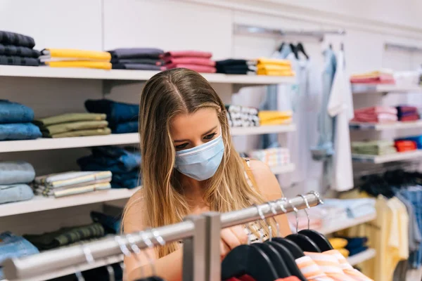 Giovane donna in maschera shopping in un negozio di abbigliamento nella pandemia coronavirus — Foto Stock