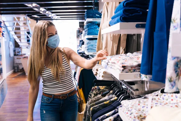 Jonge vrouw in masker winkelen in een kledingwinkel in de coronavirus pandemie — Stockfoto