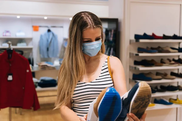 Jonge vrouw in masker winkelen in een kledingwinkel in de coronavirus pandemie — Stockfoto