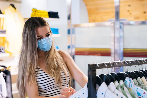 Jonge vrouw in masker winkelen in een kledingwinkel in de coronavirus pandemie — Stockfoto