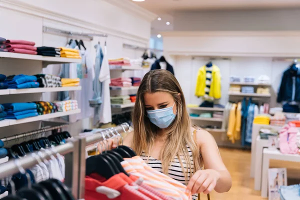 Giovane donna in maschera shopping in un negozio di abbigliamento nella pandemia coronavirus — Foto Stock