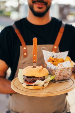 Garson, ahşap tahtalarda servis edilen lezzetli bir hamburger, patates ve sos..