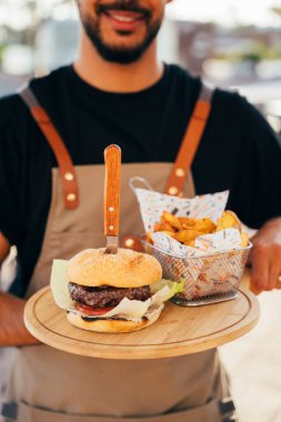 Garson, ahşap tahtalarda servis edilen lezzetli bir hamburger, patates ve sos..