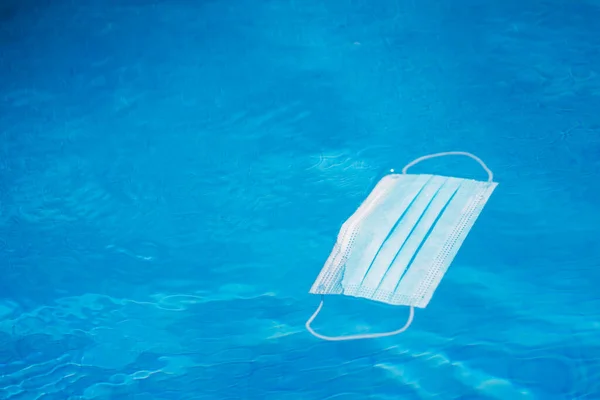 Маска, плавающая в воде бассейна во время пандемии Ковида. — стоковое фото