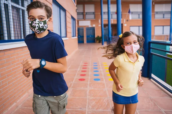 Torniamo a scuola. Bambini che corrono nel cortile della scuola con maschera facciale — Foto Stock