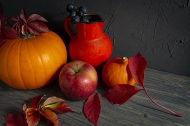 Parlak sonbahar ile iki kabaklar bir siyah kaba beton grunge duvara ahşap rustik masa üzerinde elma, üzüm ve kırmızı sürahi bırakır. Ücretsiz kopya alanı ile sonbaharda hasat ve tatil natürmort