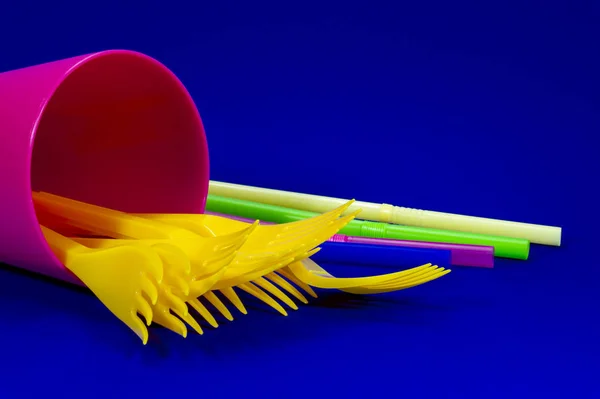 A pile of yellow plastic forks in a plastic pink mug and colored straws on blue background