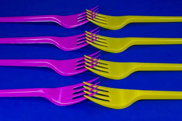 黄色とピンクの食器プラスチック フォーク青色の背景上に配置 色彩動向プラスチック廃棄物問題のコンセプト — ストック写真
