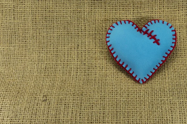 Valentine Day template, one handmade blue foam sheet stitched toy heart on jute canvas, close up, high angle view. Love, relationship, Valentines Day, broken heart and gay love concept