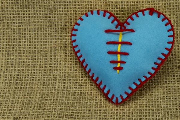 Valentine Day template, one handmade blue foam sheet stitched toy heart on jute canvas, close up, high angle view. Love, relationship, Valentines Day, broken heart and gay love concept