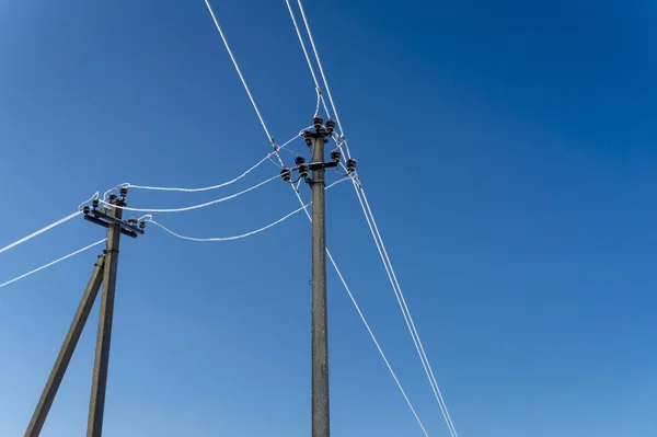 Two electric line poles with frozen wires in winter, viewed from low angle against clear blue sky