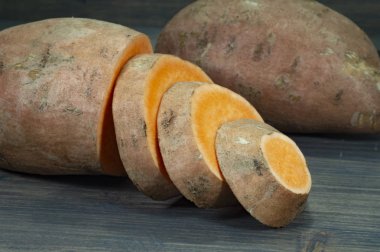 Bütün ve dilimlenmiş tatlı patates Ipomoea batatas içinde karanlık rustik masa arka plan üzerinde yakın çekim