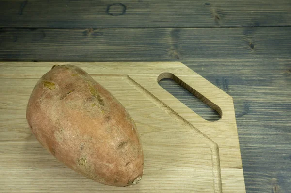 Batata doce inteira em uma tábua de corte de madeira — Fotografia de Stock