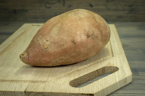 Batata doce inteira em uma tábua de corte de madeira — Fotografia de Stock