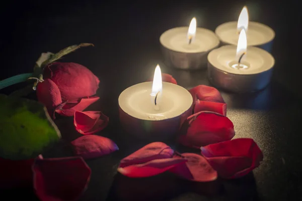 Quatro velas de chá e pétalas de rosa no escuro — Fotografia de Stock