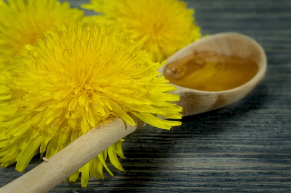 Mel em colher de madeira e dente-de-leão de primavera amarelo — Fotografia de Stock