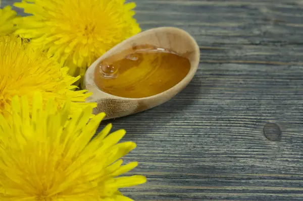 Miel en cuchara de madera y diente de león amarillo de primavera — Foto de Stock