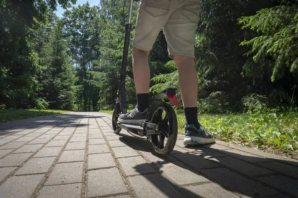 Підліток їде чорний скутер на дорозі в парку — стокове фото