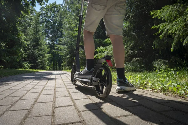 Adolescente equitação preto chute scooter na estrada no parque — Fotografia de Stock