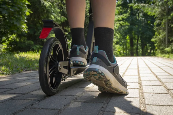Adolescente cabalgando negro patada scooter en camino en parque —  Fotos de Stock