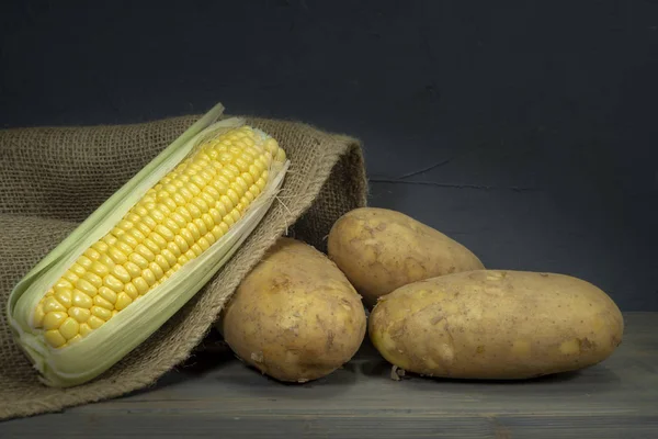 Potatoes and corncobs spilling out of hessian sack — Stock Photo, Image