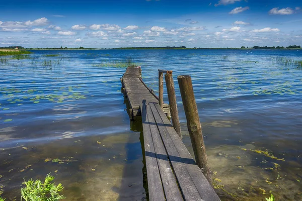 Gamla rangliga träbrygga som leder in i en sjö — Stockfoto