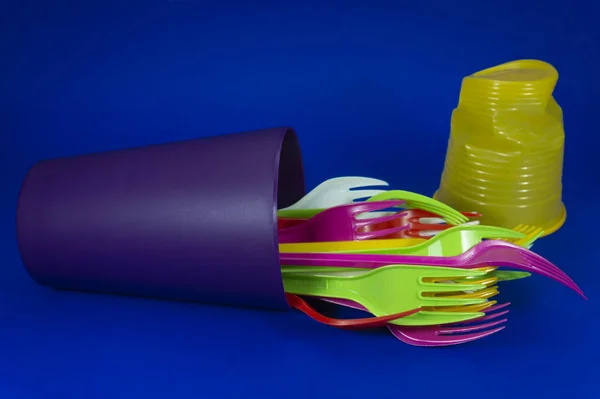 Plastic forks, mug and straws on blue background