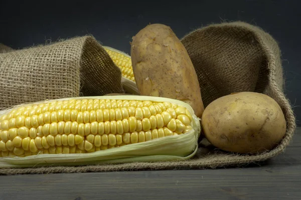 Potatoes and corncobs spilling out of hessian sack — Stock Photo, Image