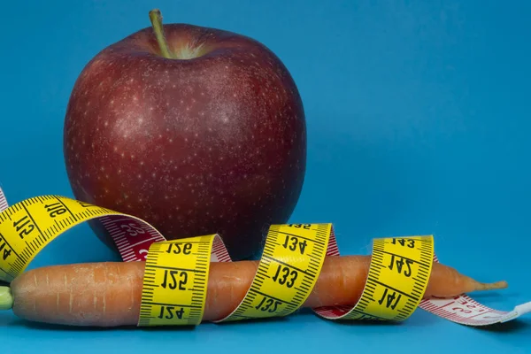 Measuring tape carrot and apple on blue background