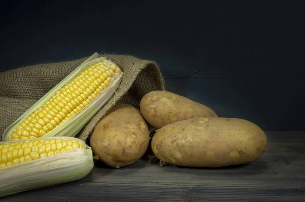 Potatoes and corncobs spilling out of hessian sack — Stock Photo, Image