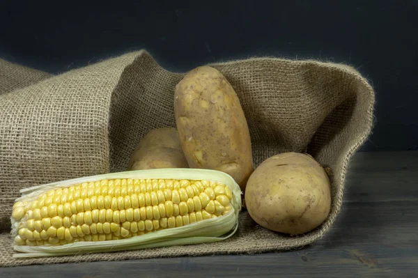 Potatoes and corncobs spilling out of hessian sack — Stock Photo, Image