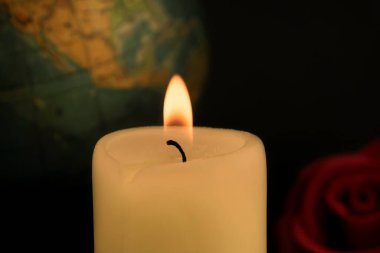 Küresel felaketler ve ölümler kavramına karşı kırmızı ve sarı güllerin yanında yanan tek bir sarı mum.