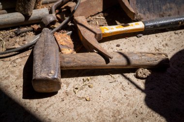 Ön planda çekiç ve çekiçle eski tozlu bir tezgahta duran paslı aletler.