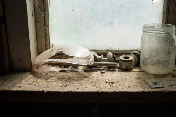 窓の前に空のガラス瓶とほこりの多い木製の作業台の上に古いツールと安全ゴーグル — ストック写真