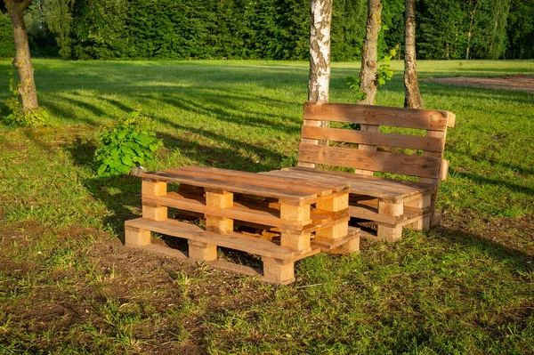 Outdoor furniture made from wood pallets surrounded by trees and greenery in summer sunshine