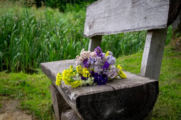 Posy of fresh spring flowers on a rustic weathered wooden bench outdoors in a park with a background of greenery conceptual of the season