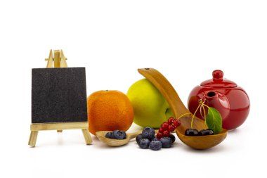 Taze mevsimlik meyveler, küçük karatahta ve yabanmersini, kiraz ve kırmızı frenk üzümlü ahşap kaşıklarla elma, turuncu ve renkli kırmızı çaydanlıklarla dolu çeşitli meyveler.
