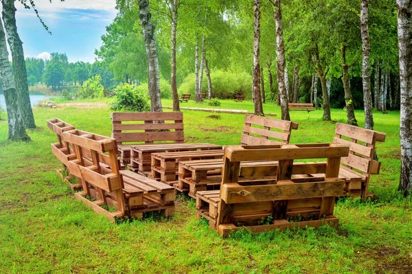 Outdoor furniture made from wood pallets surrounded by trees and greenery in summer sunshine