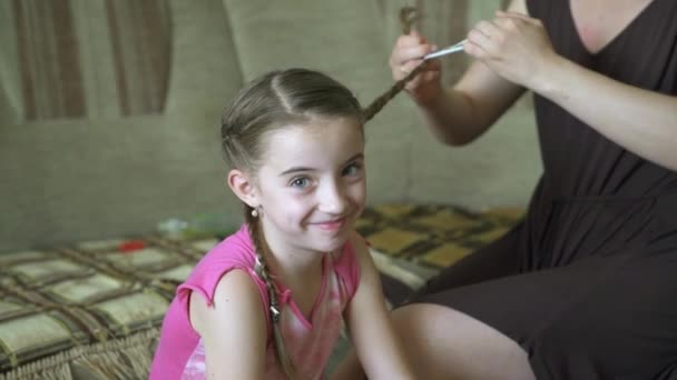 Le mani delle donne fanno acconciatura per la sua figlioletta. Una donna sta intrecciando i capelli per sua figlia . — Video Stock