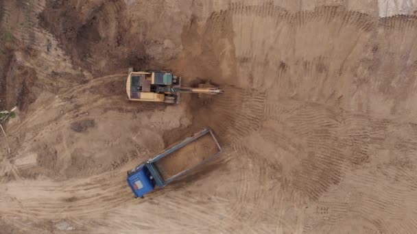 Antenn ovanifrån: gul grävmaskin häller jord i tipper. — Stockvideo